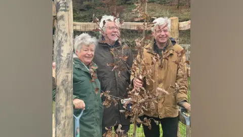 BBC Three people stood behind newly planted tree