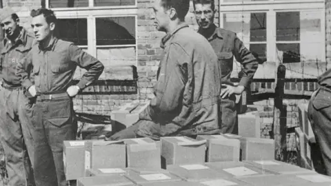 Bettmann/Getty A black and white World War Two picture of prisoners of war next to small cardboard boxes with food in them