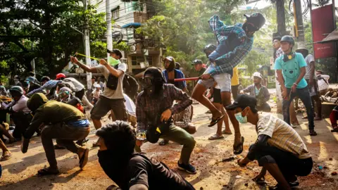 Getty Images Anti-coup protesters use slingshots and pelt stones towards approaching security forces in Yangon, March 2021