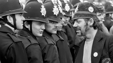 Martin Jenkinson Image Library Picket wearing a joke police helmet talking to officers without identification numbers at Orgeave