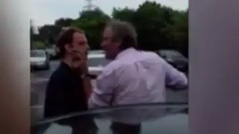 Louise Small A man is held around the neck while another man threatens him