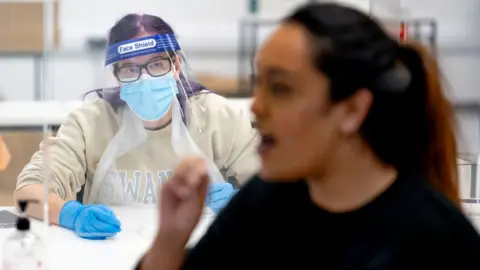 Getty Images A medical staff looks on as a student inserts a swab into her mouth as part of a COVID-19 lateral flow test at Swansea University on December 8, 2020 in Swansea, Wales.