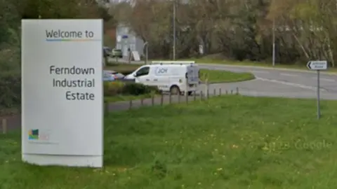 Entrance to Ferndown Industrial Estate, complete with a big silver sign next to the road.