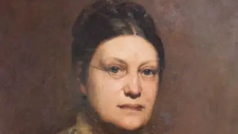 University of Manchester Painting of Lydia Becker who has brown hair in a bun and is wearing round spectacles. 