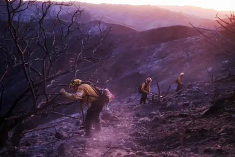 David Swanson/Reuters Three firefighters work to extinguish remaining embers in a charred landscape in LA. 