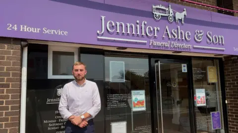 A man standing in front of a purple funeral directors sign