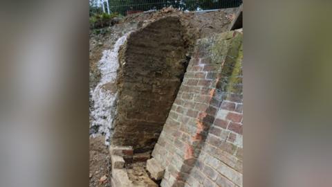 Image of a collapsed brick wall along a canal path