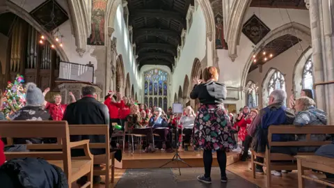 Sounds Better CIC A church setting with people singing with Christmas jumpers on