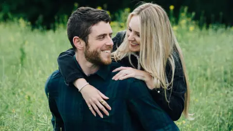 Martis Media Andrew and Lissie Harper. She is standing in front of her looking back as she wraps her arms round his shoulders. Both are smiling