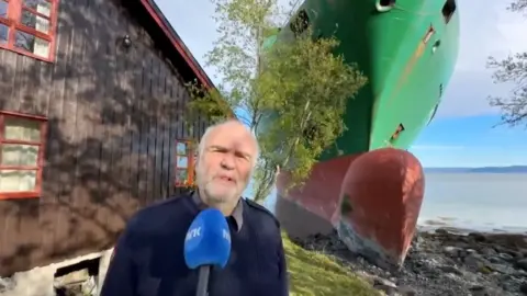 Johan Helberg stood in his garden speaking into a microphone, with the ship behind him