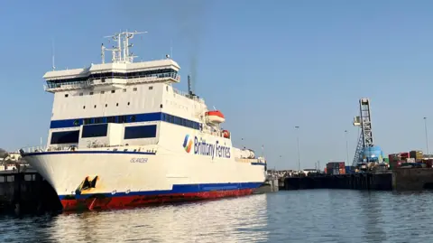 A front view of the large white Islander vessel with its blue and red trim. 
