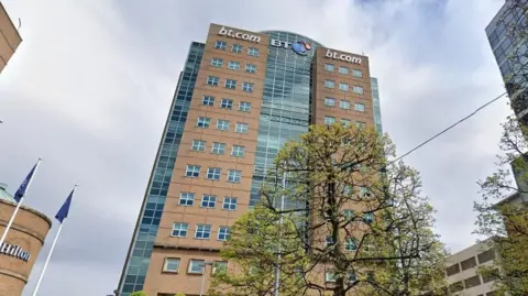 A tall office block with sand coloured panelling and windows. It says BT.COM at the top