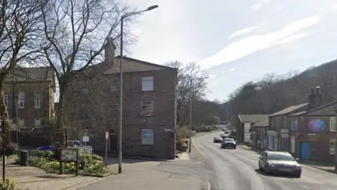 Google Crawshawbooth - junction of York Street and Burnley Road.
A small public square is on the left, with a stone-built three-storey building on the street corner opposite a terrace of small shops.