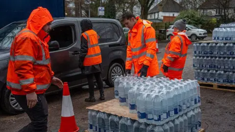 Getty Images Four people in hi-vis orange jackets taking out bottled water supplies out of vehicles at a carpark.
