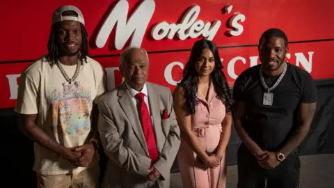 London Museum Musicians Krept and Konan (far left and right) stand with Sydenham Morley’s manager Kannalingam Mahendran and his daughter Janani Nageswaran, with the original Morley’s sign visible behind them.