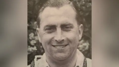 BBC Black and white portrait of Harold Gimblett wearing a white shirt and sweater and smiling. 