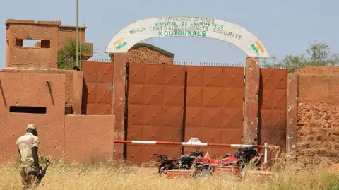 A Nigerien soldiers walks near calcined motorcycles used by assailants, in front of the the prison of Koutoukale, near Niamey, following an attack on October 17, 2016.