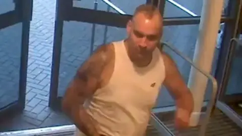 Piotr Huczynski, man in a sleeveless white top, at hospital entrance doors, in a CCTV image