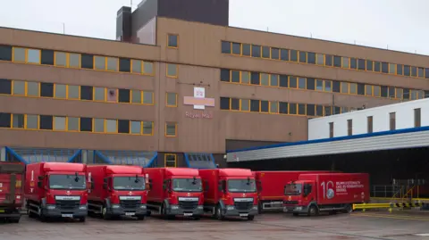 Getty Images A row of red postal lorries are lined up outside Cardiff sorting office. The building has brown cladding on and horizontal rows of windows with the Royal Mail insignia on the front.