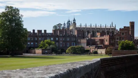 Getty Images Eton College seen from a distance. It's a large red brick building with multiple spires and turrets, with a well-kept lawn next to it.