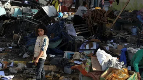 Reuters A young girl stands in the rubble of a building, surrounded by debris, broken furniture and clothing