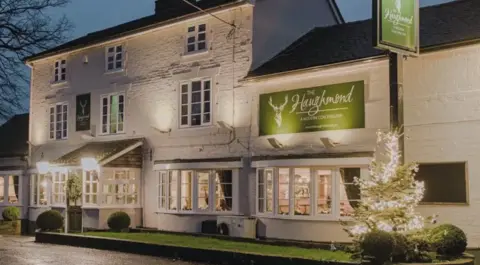 A large white building with a brown tiled roof and large bay windows and two green signs which both read The Haughmond