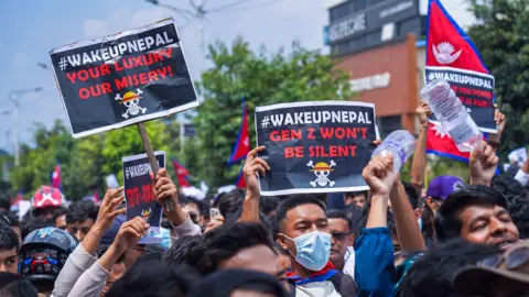 Getty Images Some among a crowd of people hold up placards that read "#WakeUpNepal Gen Z won't be silent". There's a Nepali flag in the background towards the right of the picture