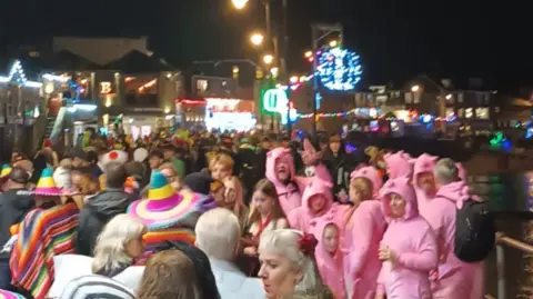 St, Ives Business Improvement District People pack the harbour front in fancy dress, A group of people stand next to the sea dressed as pigs , several partygoers wear Mexican hats and ponchos.