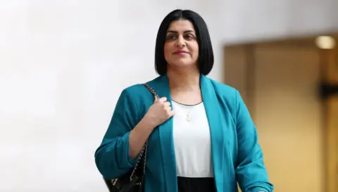  Home Secretary Shabana Mahmood arrives at the BBC in London. She is wearing a turquoise blazer and has a black handbag wrapped over her right shoulder