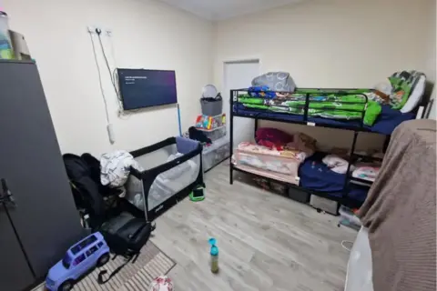 Getty Images A bedroom with a double bunk bed and a child's travel cot as well as lots of belongings stored.