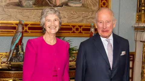 Irish president Catherine Connolly during an audience with King Charles III at Buckingham Palace in London, as part of her official visit to the UK. She has short white hair and wearing a pink dress and jacket. The king has short white hair, wearing navy blazer, white shirt and silver tie and pocket square.
