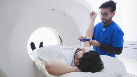 Young male radiographer preparing male patient for CT scan in radiology department 