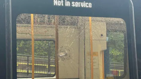 A train window with a smashed hole in the centre of it. Above a sign reads 'not in service'.