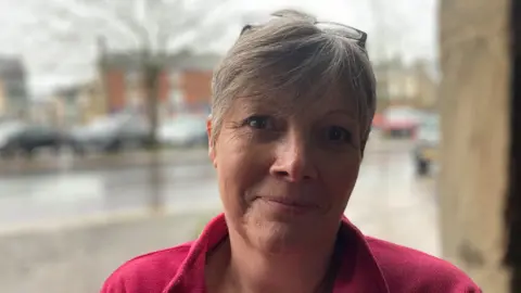 Laura Coffey/BBC A woman in a red coat looks at the camera.