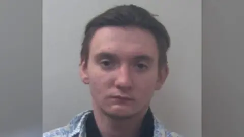 A mugshot of a man with medium-length brown hair looking at the camera.