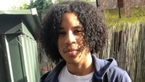 Sixteen-year-old Rhamero West poses for a photograph. He is wearing a white t-shirt and dark blue hoodie.