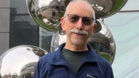 Photograph of patient Richard Nelson, who has received a new type of vaccine for bowel cancer. He's pictured outside the Christie Hospital.