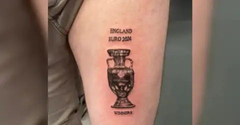 PA/DAN THOMAS A leg with a black tattoo of a trophy with the words "England Euro 2024" written above it and the word "Winners" below it. The skin around the tattoo is reddened