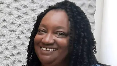 Marcia Grant smiles at the camera. She has long black curly hair.
