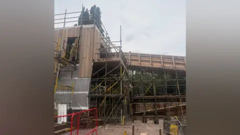 Shropshire Council A wooden structure under construction is surrounded by scaffolding. Exposed framing and protective sheeting can be seen. 