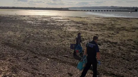 Hampshire Constabulary Two police community support officers walk across the beach towards the sea carrying three bags for life containing a haul of seafood