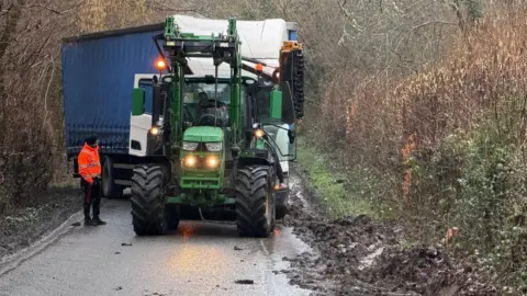 A tractor and a lorry blocking a narrow country lane