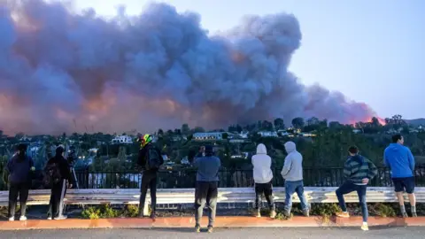 Bystanders look on as smoke billows over the LA skyline in the Pacific Palisades neighborhood on 7 January