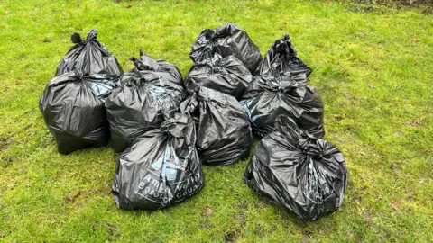 Several black bin bags full of waste on a grass verge with Amber Valley Borough Council on them