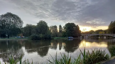 SammyJo The River Thames with a bridge over it sits almost empty aside from one boat in the distance under a low sun and dark grey clouds