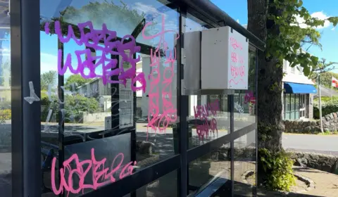 A bus shelter with pink, purple and white graffiti. its hard to make out the word but it is clearly some sort of tag
