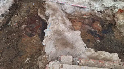 Oxford Archaeology An archaeologist's close up photo of a medieval hearth. A lighter stone structure is pictured in between darker earth, forming part of a dig at Oriel College in Oxford.