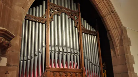 The front of the pipe organ whcih is set in a stone archway in the cathedral. It has large metal pipes standing upright held in place by ornate woodwork. 