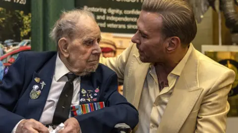 VE Day service honours last generation of WW2 veterans 12 PA Media RAF veteran Harry Winter, left, seen wearing a blue suit decorated with medals and pin badges, a white shirt and black tie, is seen next to Matt Goss, who wears a cream suit and shirt.