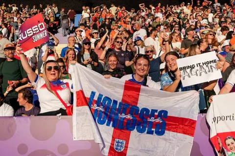 Getty Images Animated England fans cheer at the stadium holding flags and signs in support of the Lionesses.